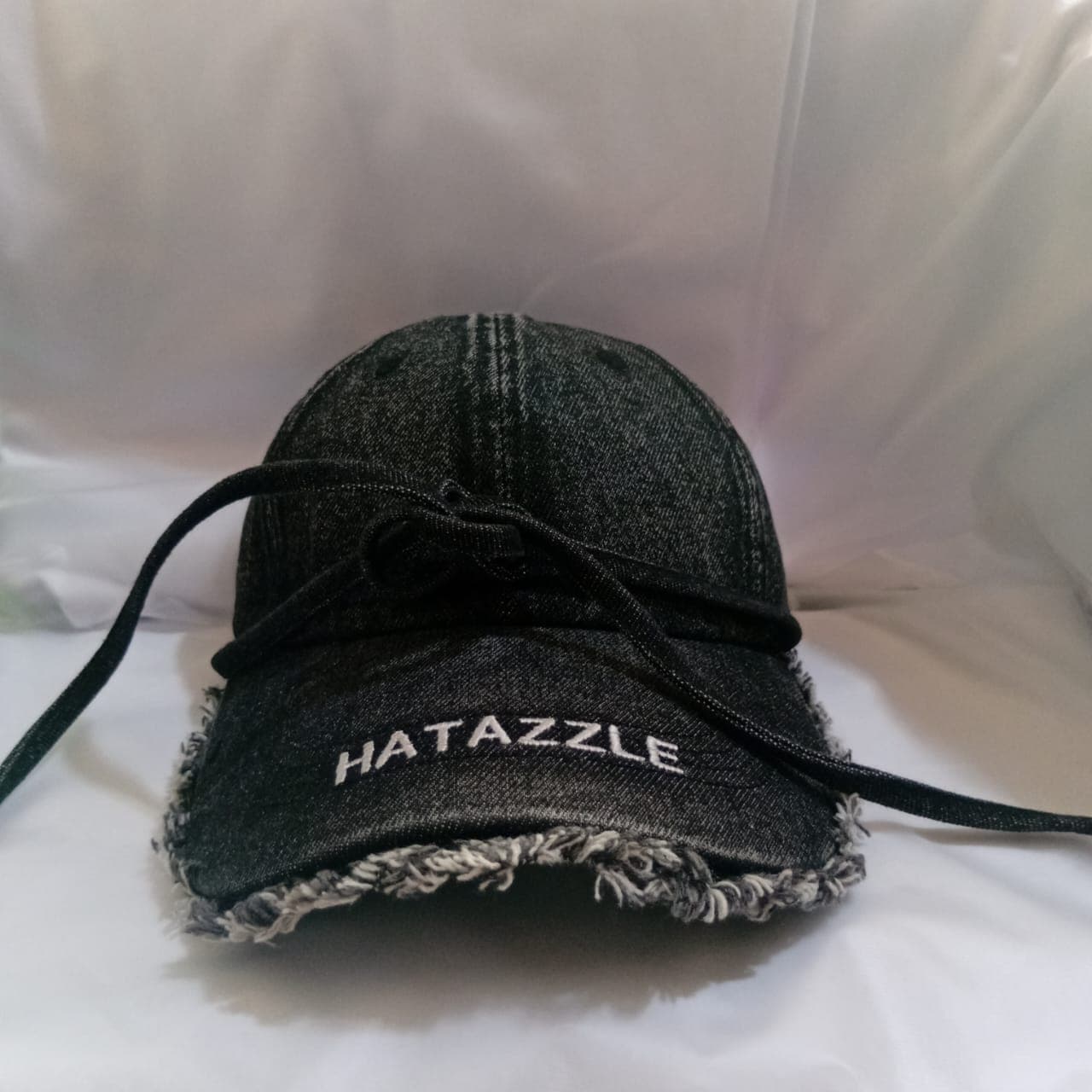 Black denim Hatazzle cap with tie strings and frayed brim.