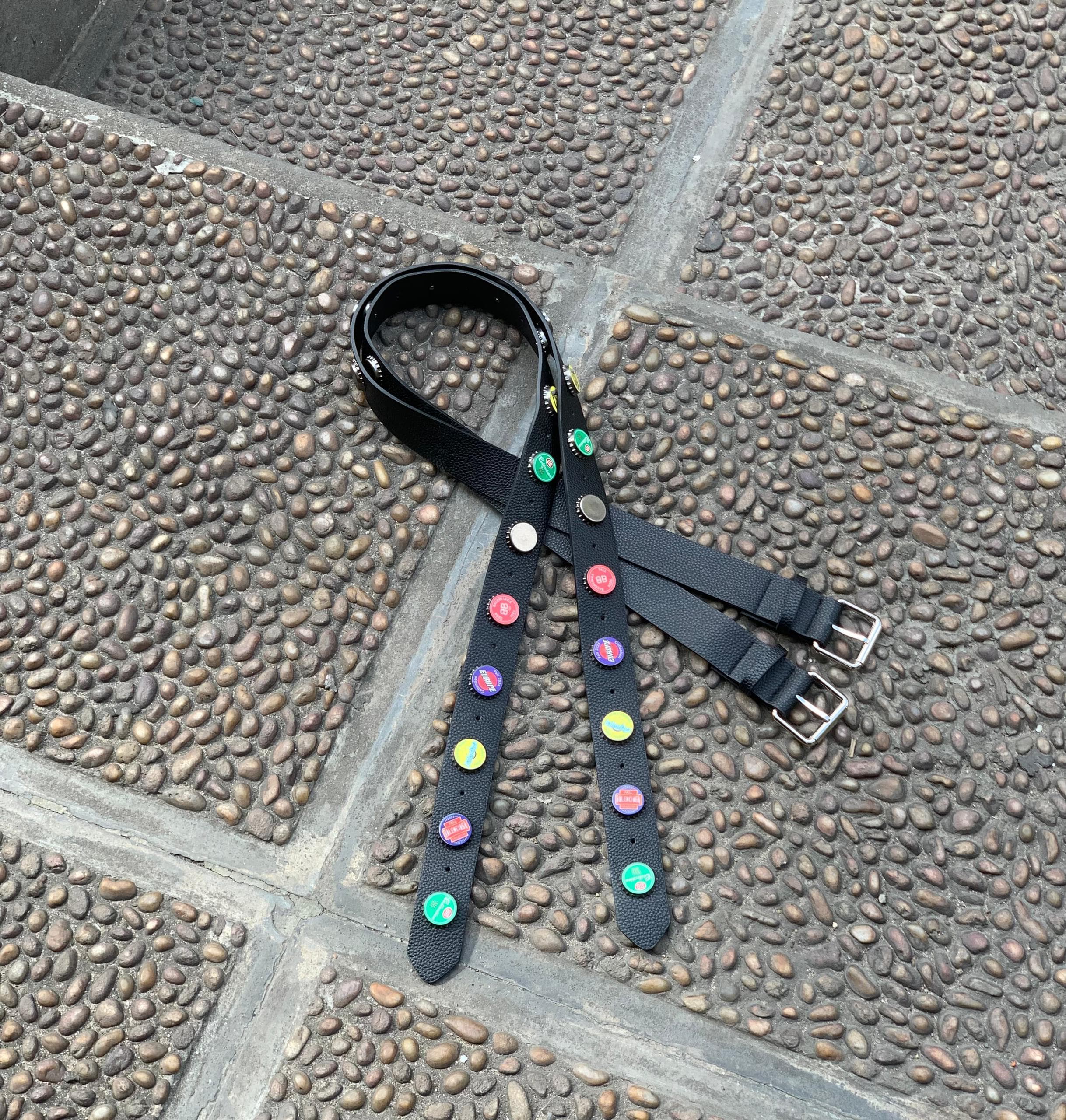 Black belt with multicolored bottle cap decorations and silver buckles laid on cobblestone.