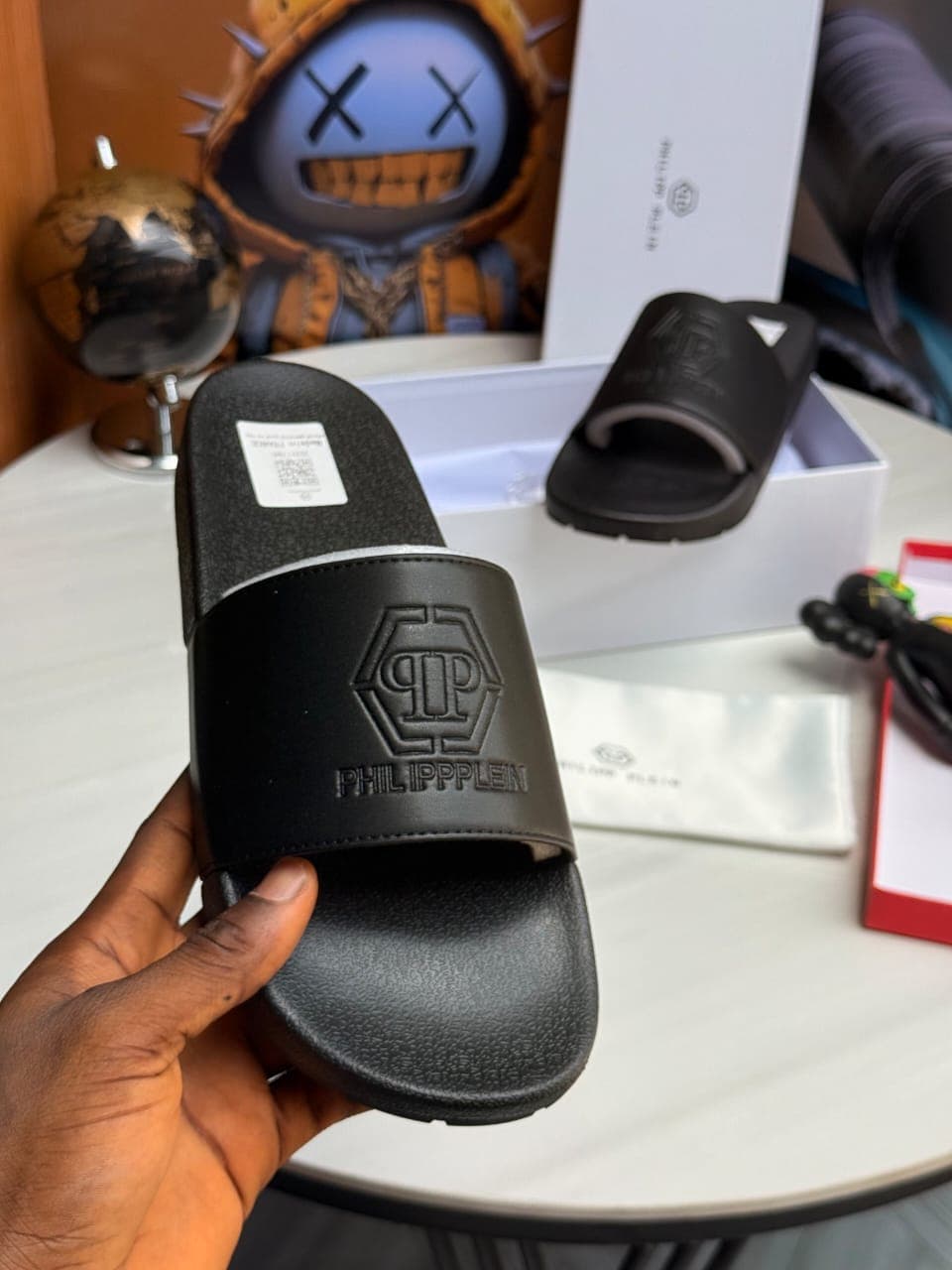 Hand holding black Philipp Plein slide with hexagon logo and text.