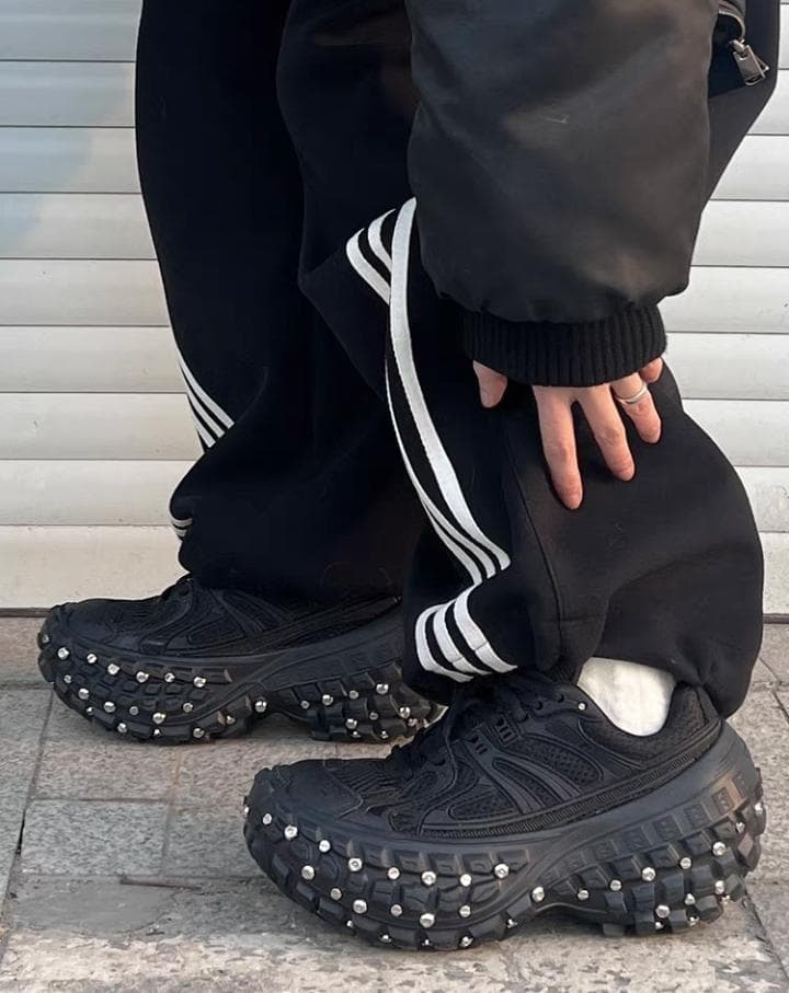 Person wearing black studded platform sneakers with black track pants.