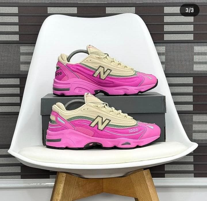 New Balance 1000 sneakers in pink with beige and green accents on white chair.