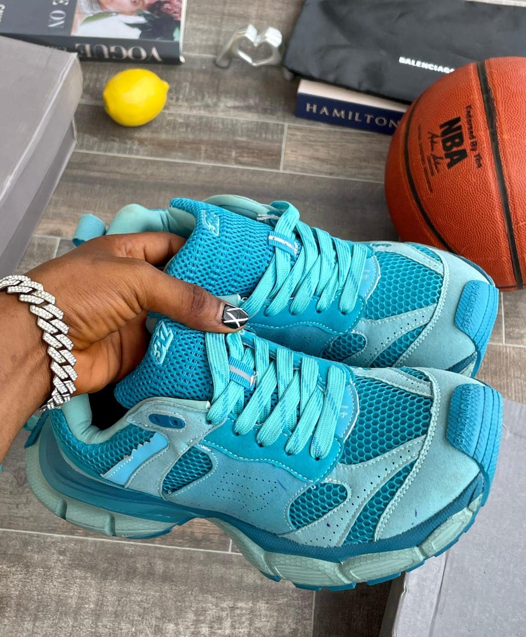 Blue New Balance sneakers held by hand with lifestyle props including basketball and books.