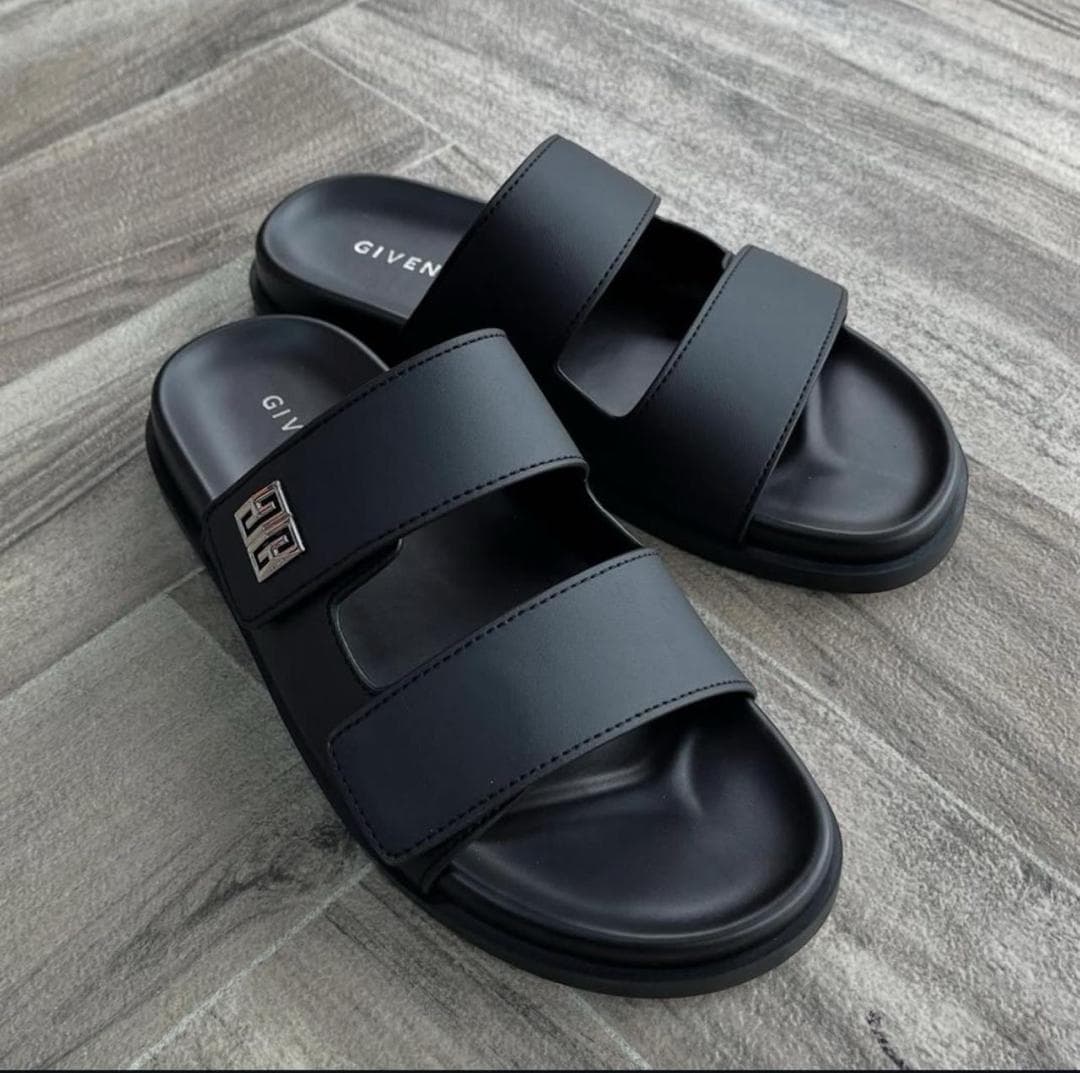 Black Givenchy double-strap slides with metal logo on gray wood floor.