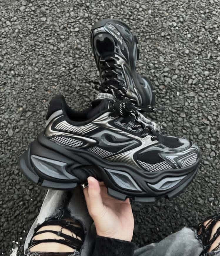 Black and silver chunky wave runner sneakers held outdoors showing detailed upper and sole.