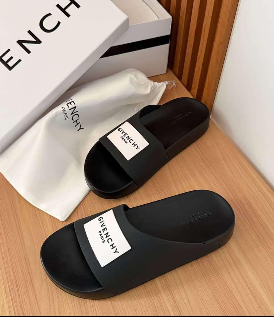 Black Givenchy slides displayed on wooden floor with white box and dust bag.