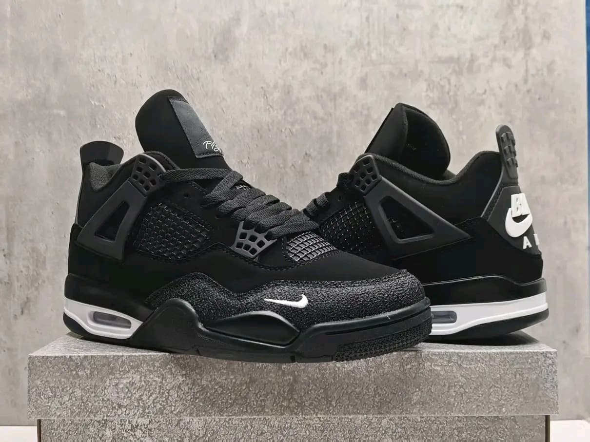 Pair of black Air Jordan 4 sneakers displayed on stone pedestal against neutral wall.