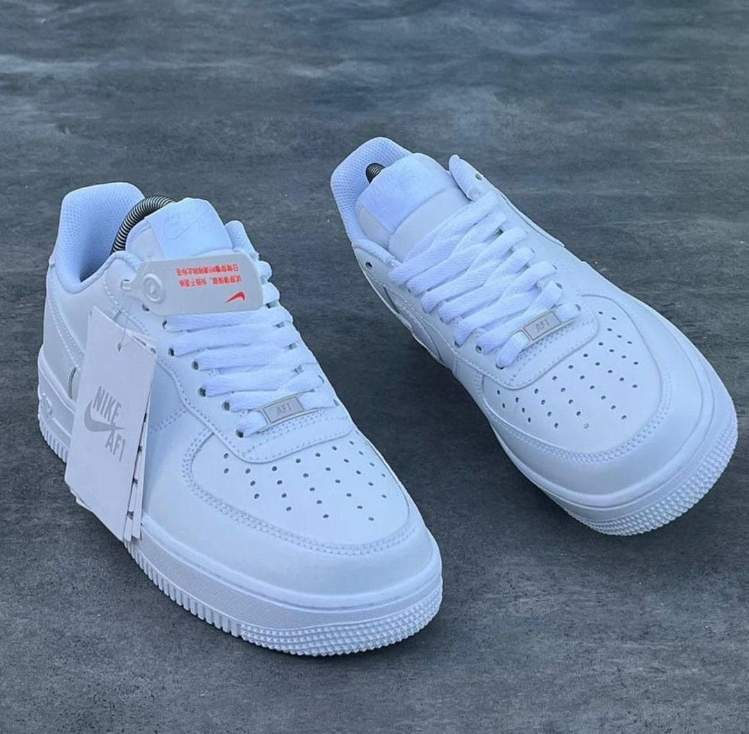 White Nike Air Force 1 sneakers on gray surface with tags attached.