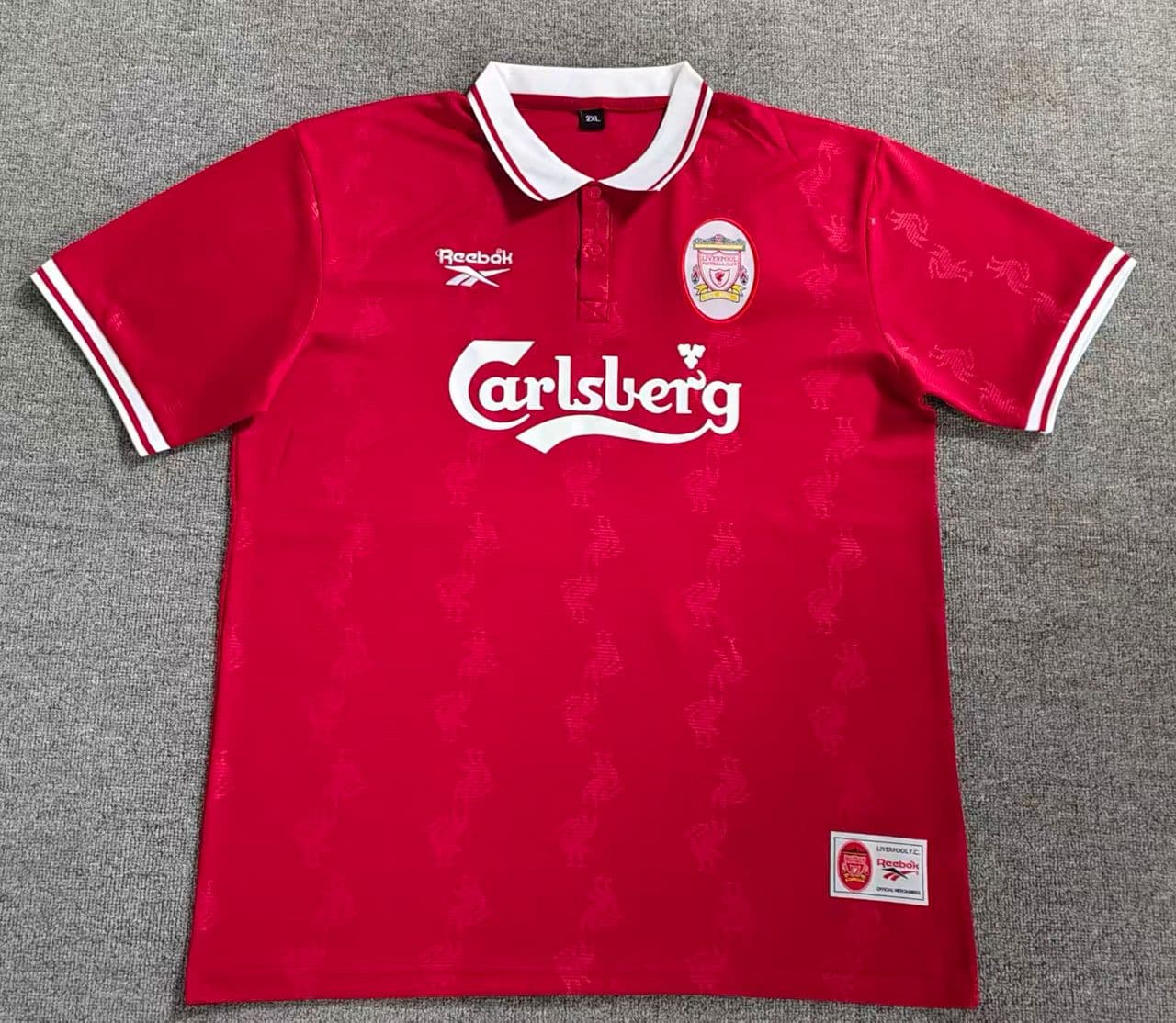 Red Liverpool soccer jersey with Carlsberg sponsor laid flat on gray background.