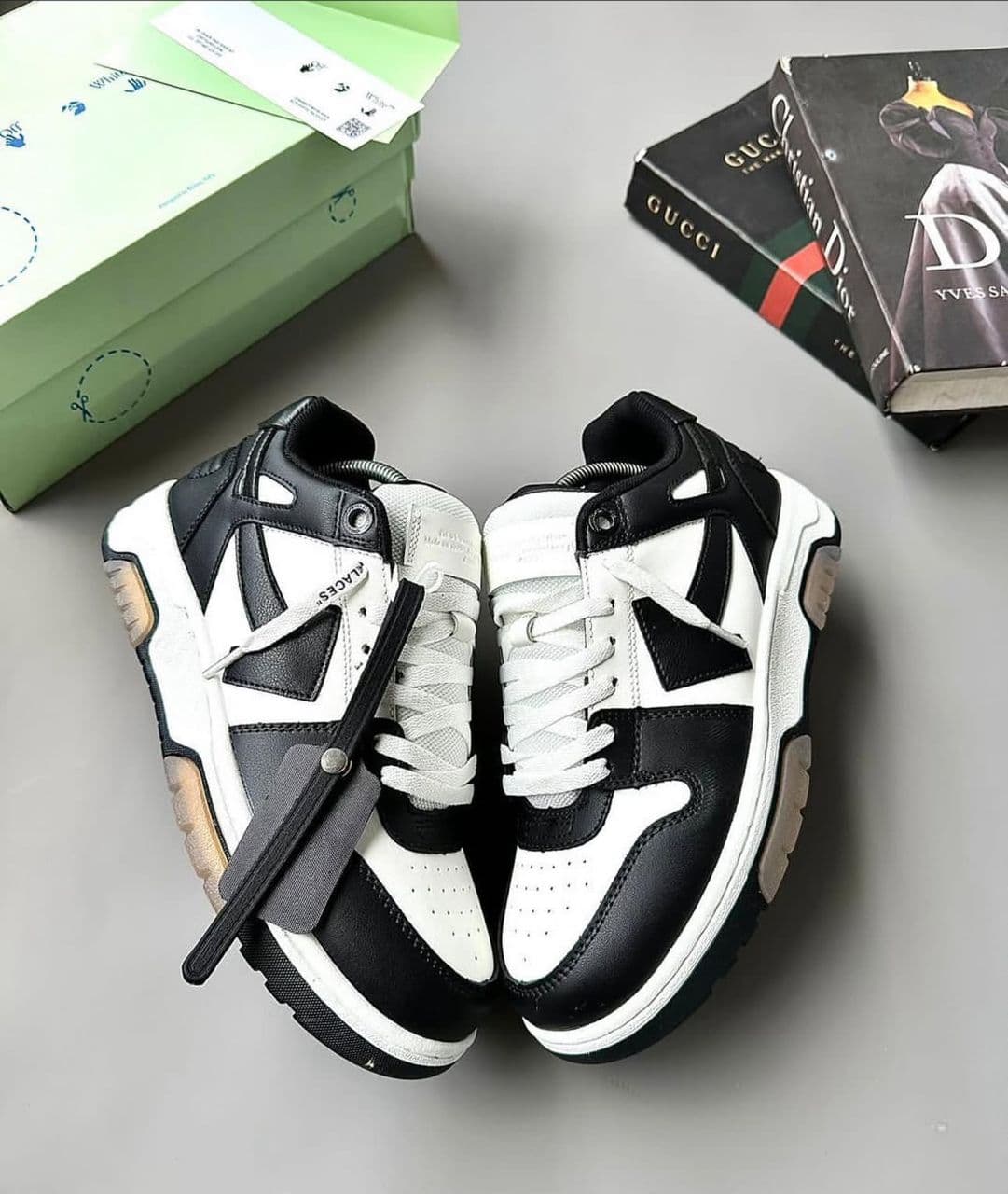 Black and white chunky sneakers with mixed materials and zip tie on gray background with green box and books.