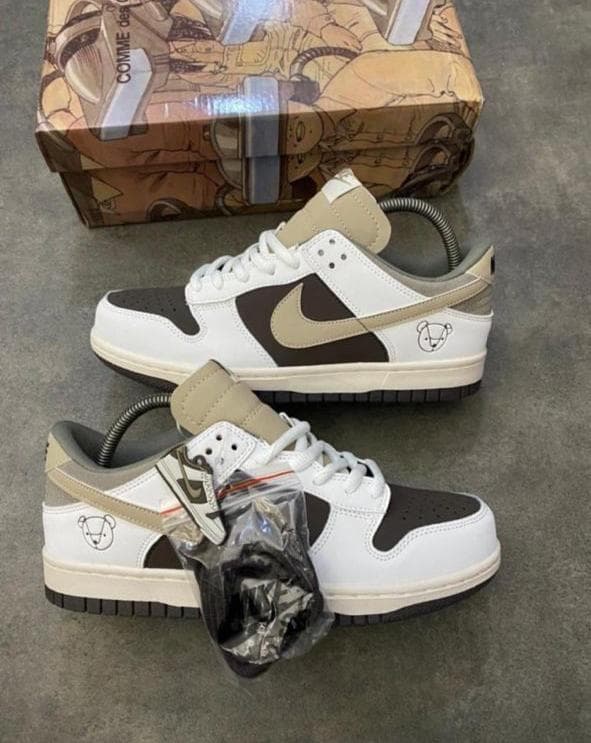Nike Dunk Low sneakers in white with brown panels, beige swoosh and bear logo detail.
