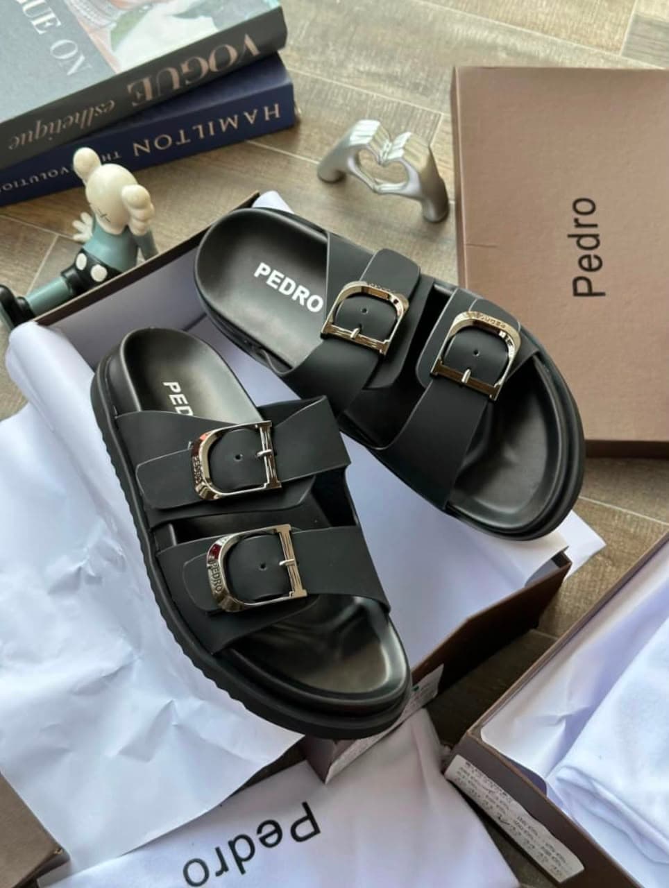 Black Pedro double-buckle slides in box with books and decorative items.