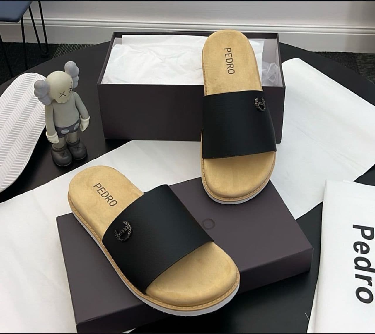 Black Pedro single-strap slide with logo, displayed with packaging, tissue and figurine.