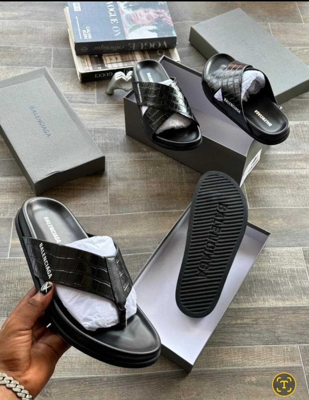 Black Balenciaga croc embossed flip flops held in hand with box and another style visible.