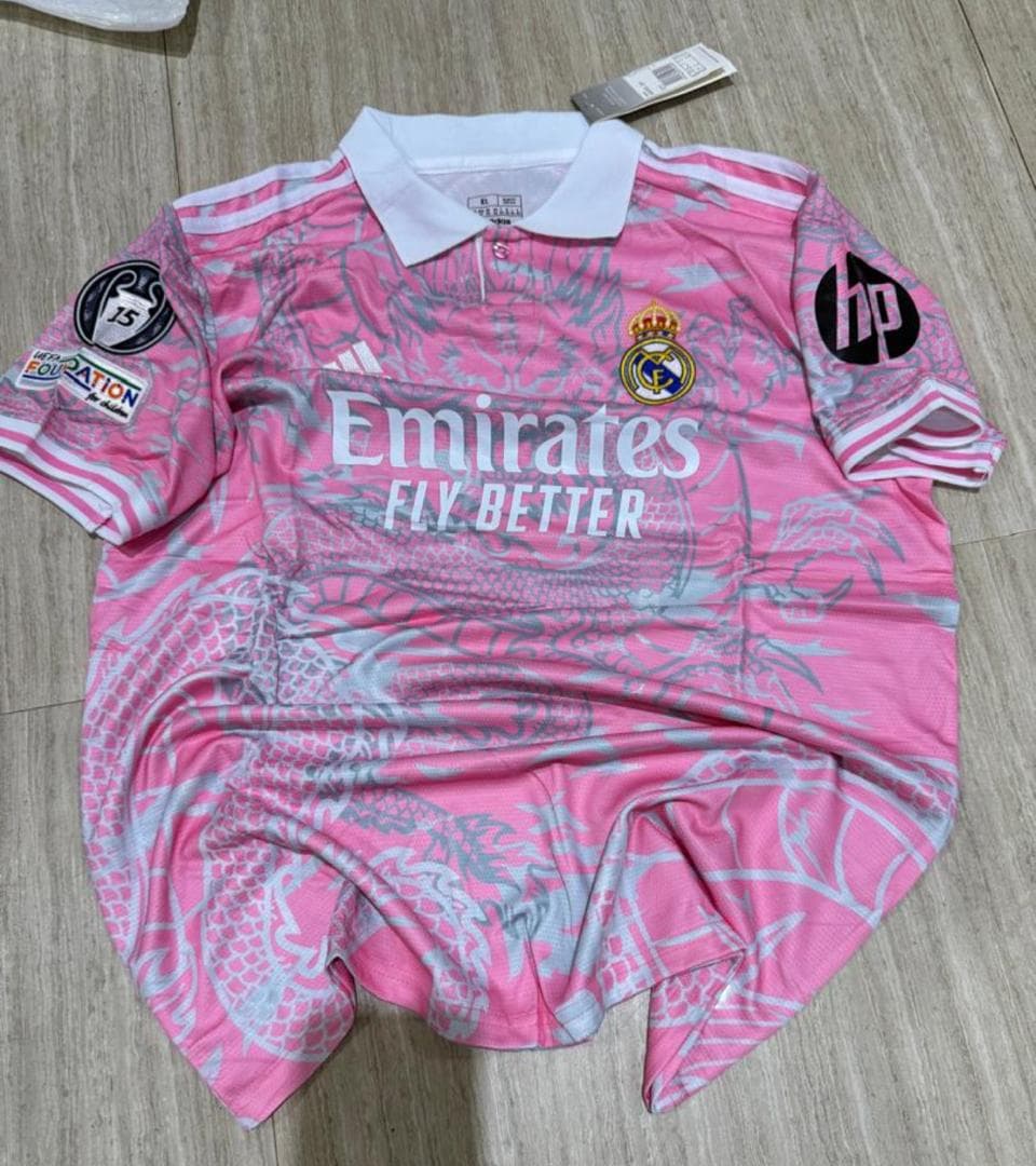 Pink Real Madrid adidas jersey with dragon pattern laid flat on wooden floor.