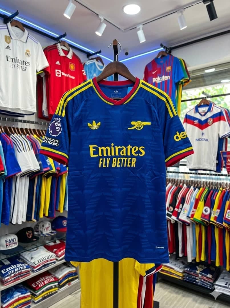 Blue Adidas Arsenal jersey with yellow shorts on hanger in shop.