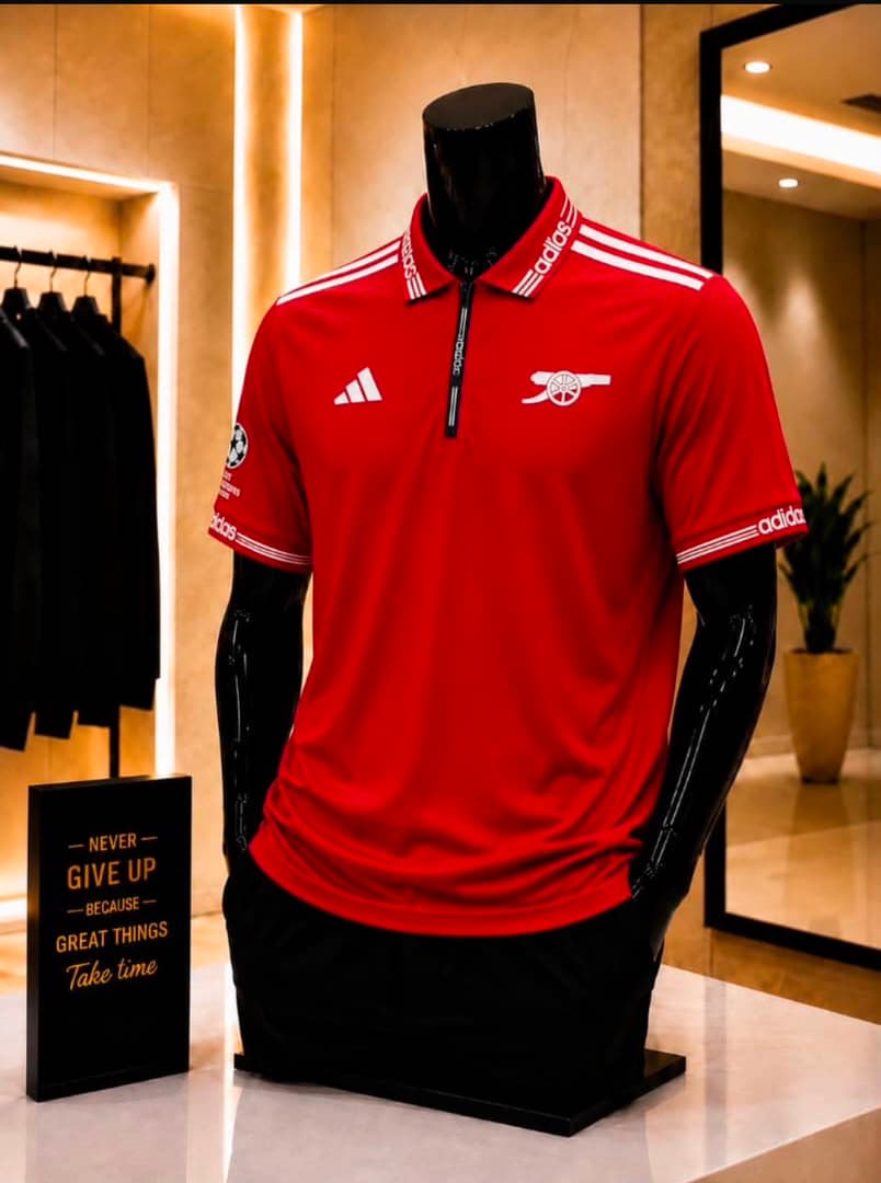 Red Adidas Arsenal polo jersey on black mannequin in store.