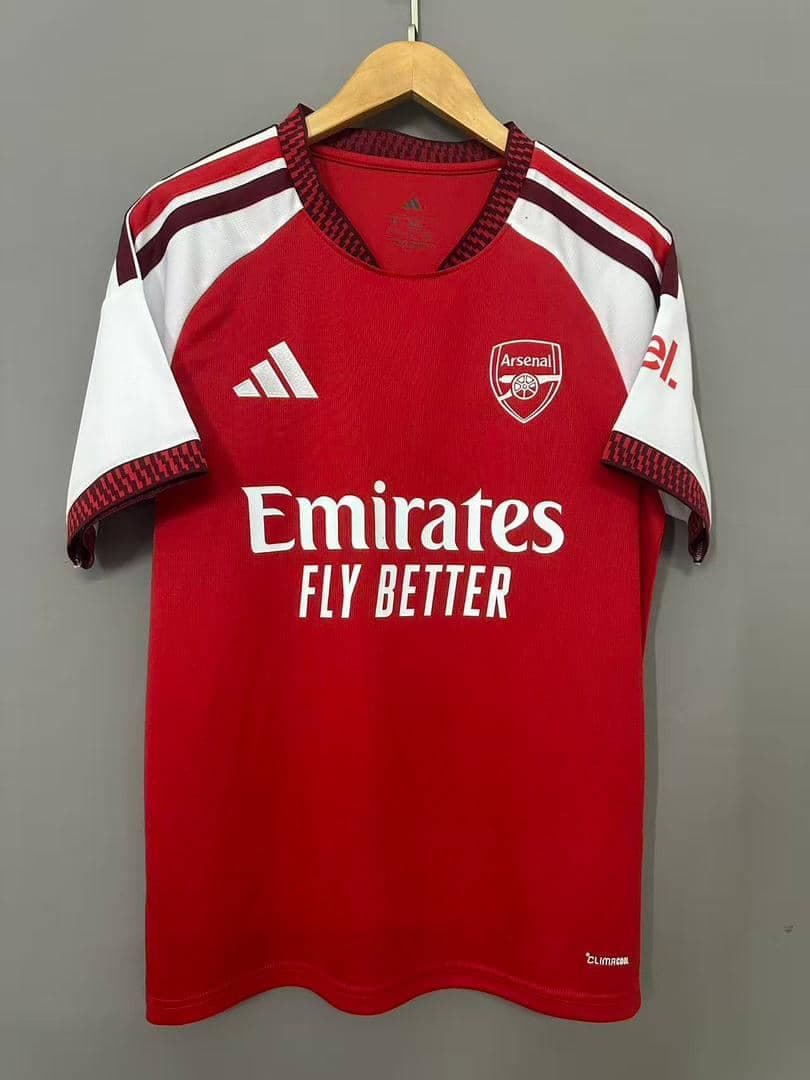Red and white Arsenal Adidas home jersey hanging on wooden hanger.