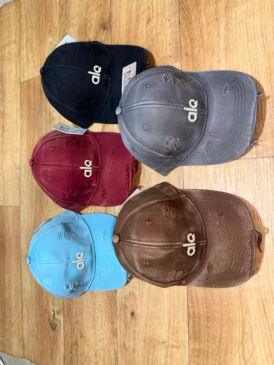 Distressed Alo logo baseball caps in black, gray, maroon, light blue, and brown.