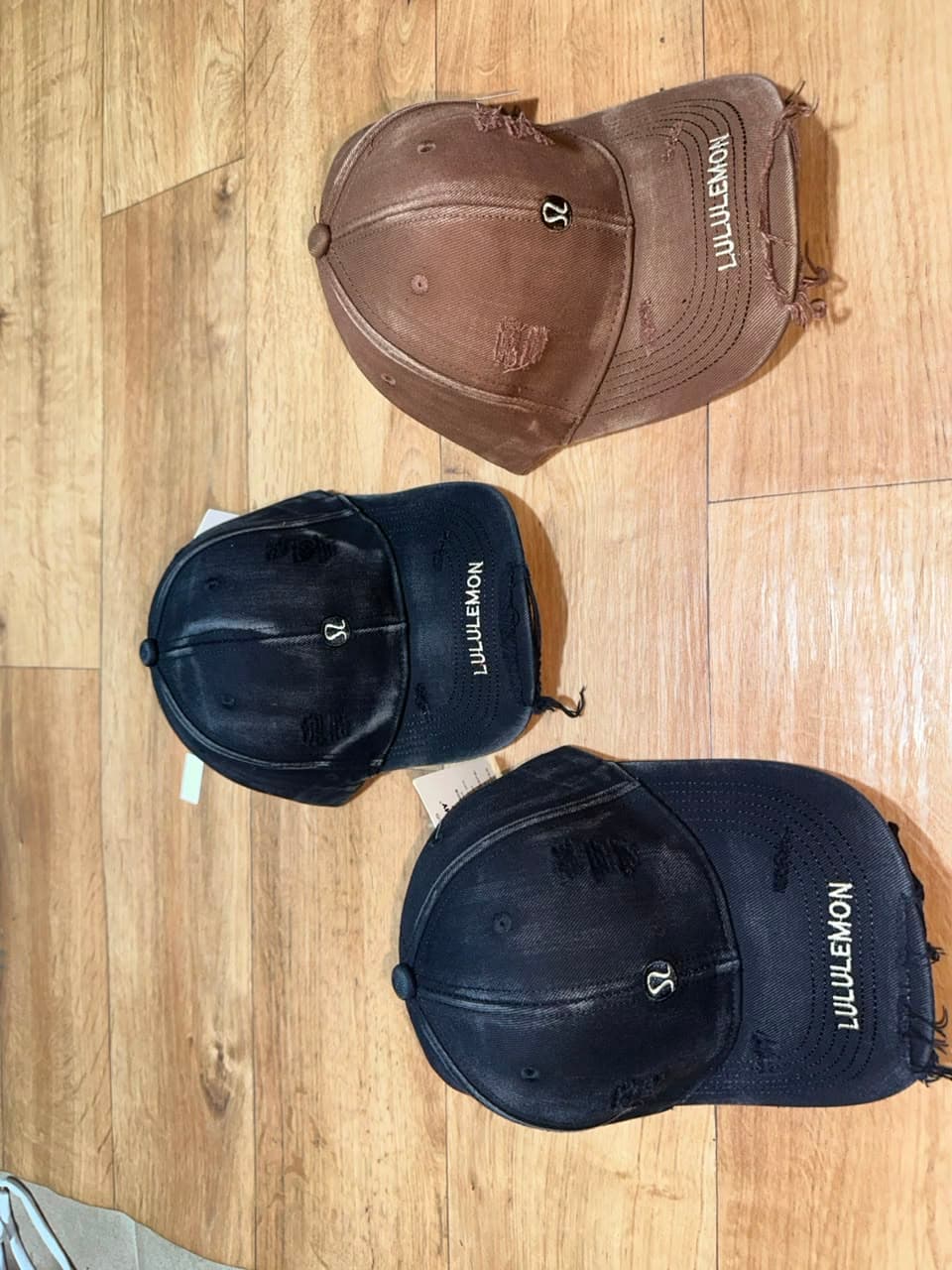 Lululemon distressed baseball caps in brown and black with logos and frayed edges.