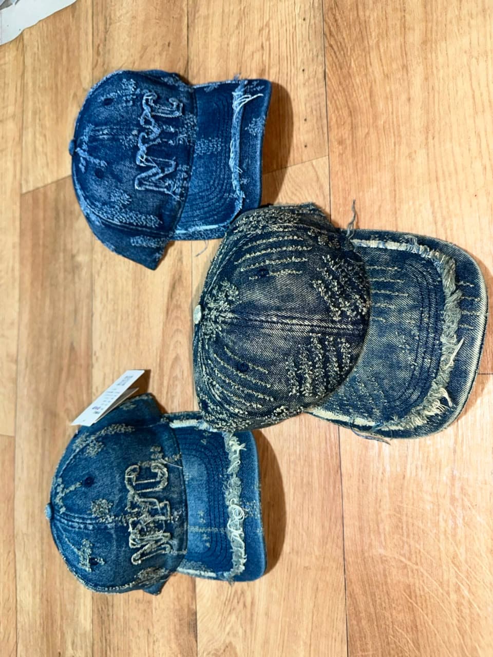 Distressed blue denim baseball caps with NYC embroidery and frayed edges shown from multiple angles.