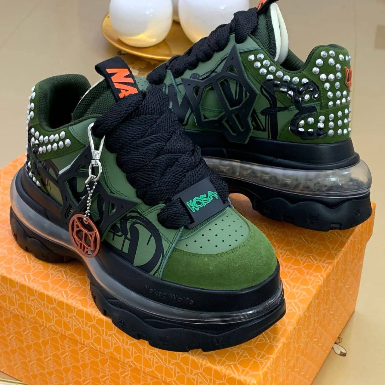 Green Naked Wolfe sneakers with studs and charms on orange box.