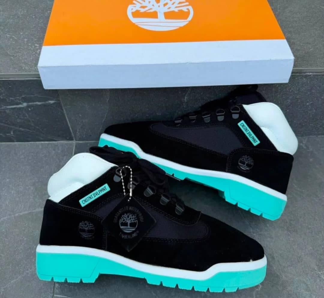 Timberland black sneakers with turquoise sole and orange box on tiled surface.
