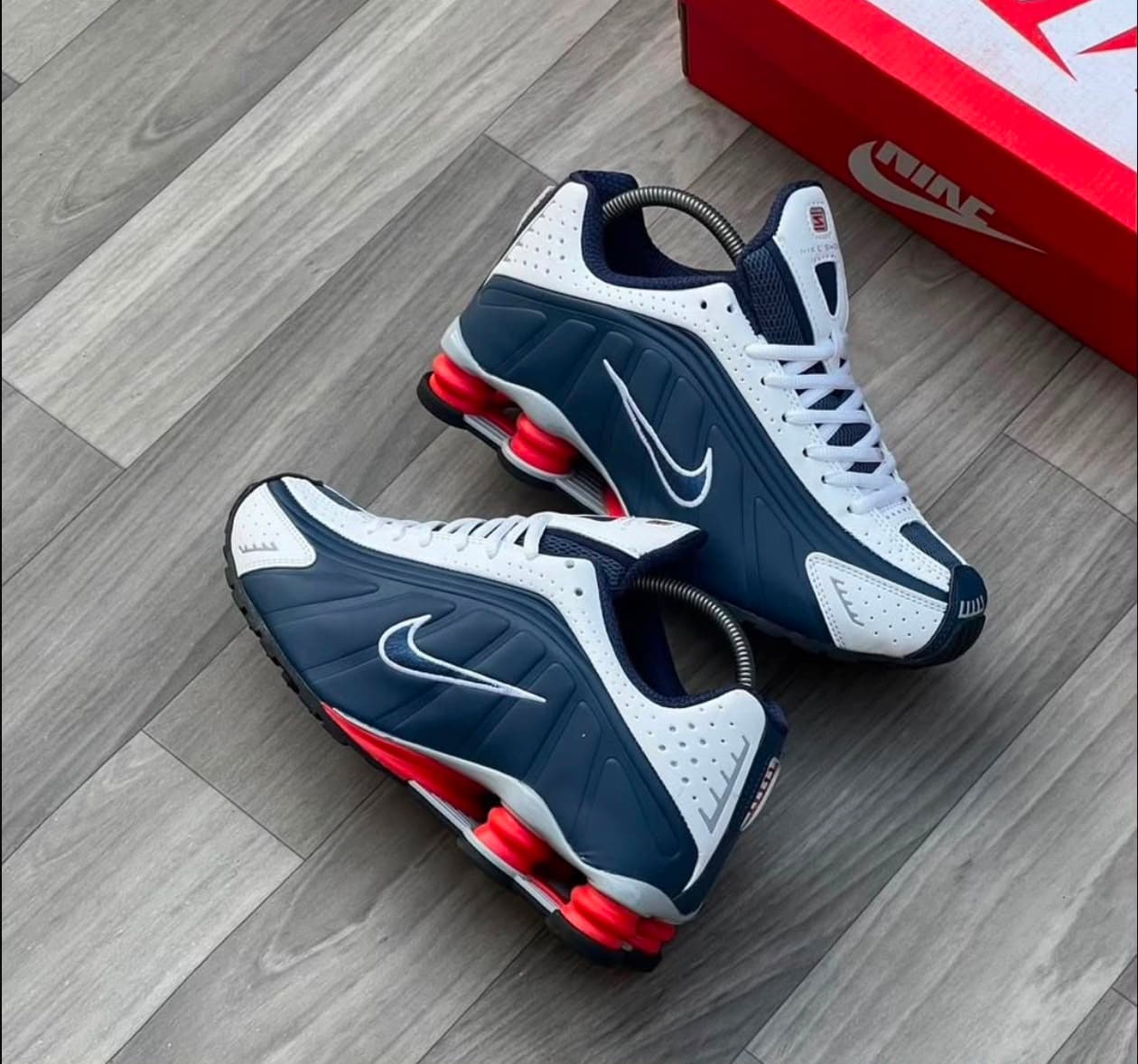 Nike Shox navy white and red sneakers on gray wood floor with red box.