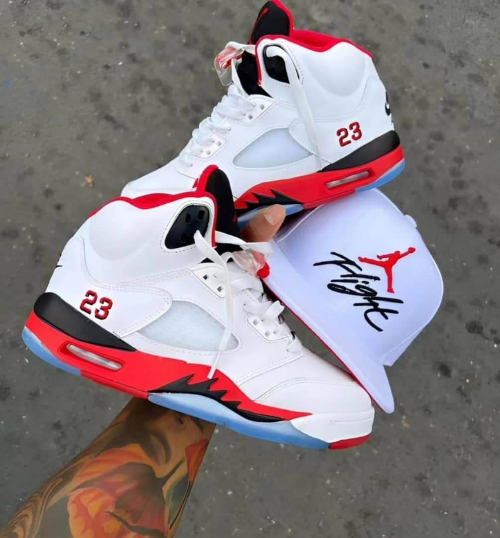 White red and black Air Jordan 5 sneakers held with a white Flight cap.