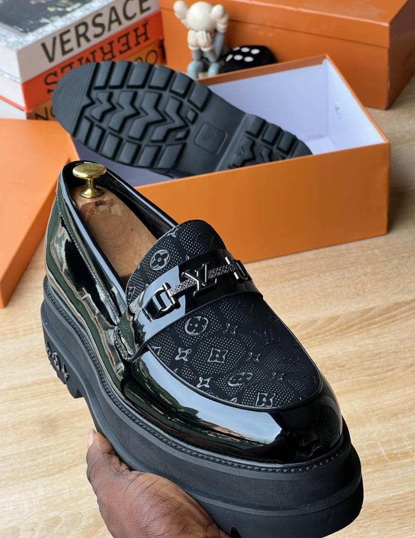 Close-up of black LV monogram platform loafer held by hand showing glossy upper and tread sole.