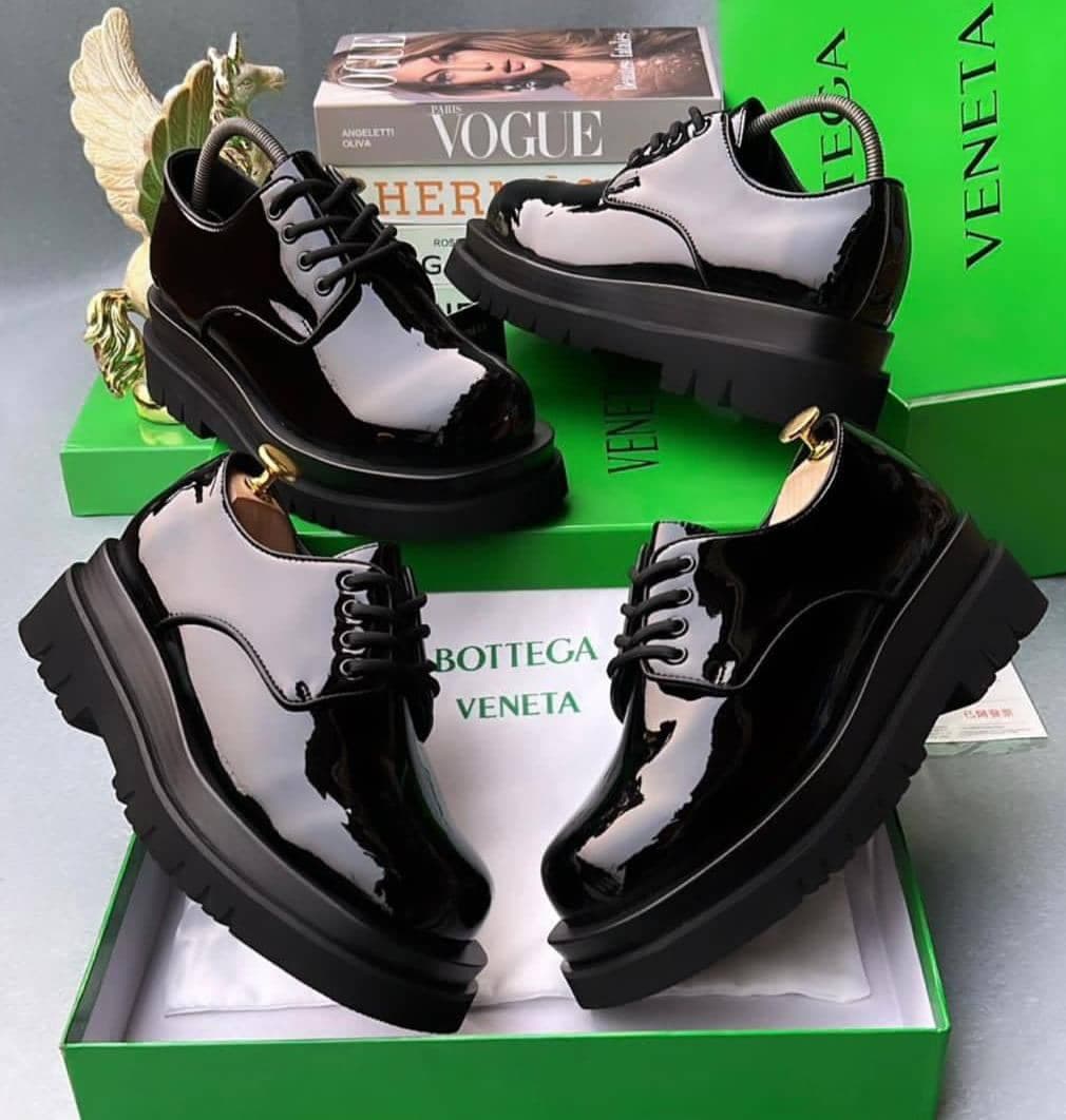 Multiple angles of black patent leather platform derby shoes displayed with luxury boxes and decor.