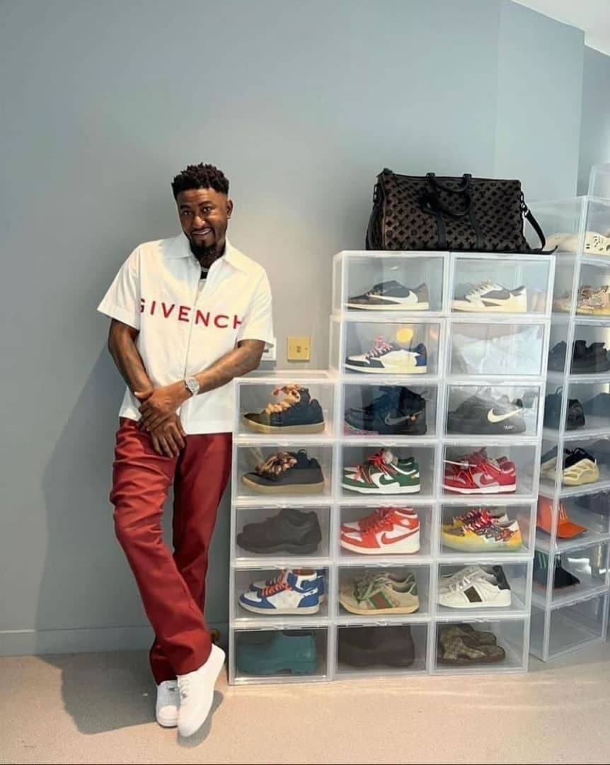 Man standing next to multiple stacks of clear acrylic shoe boxes filled with various sneakers.