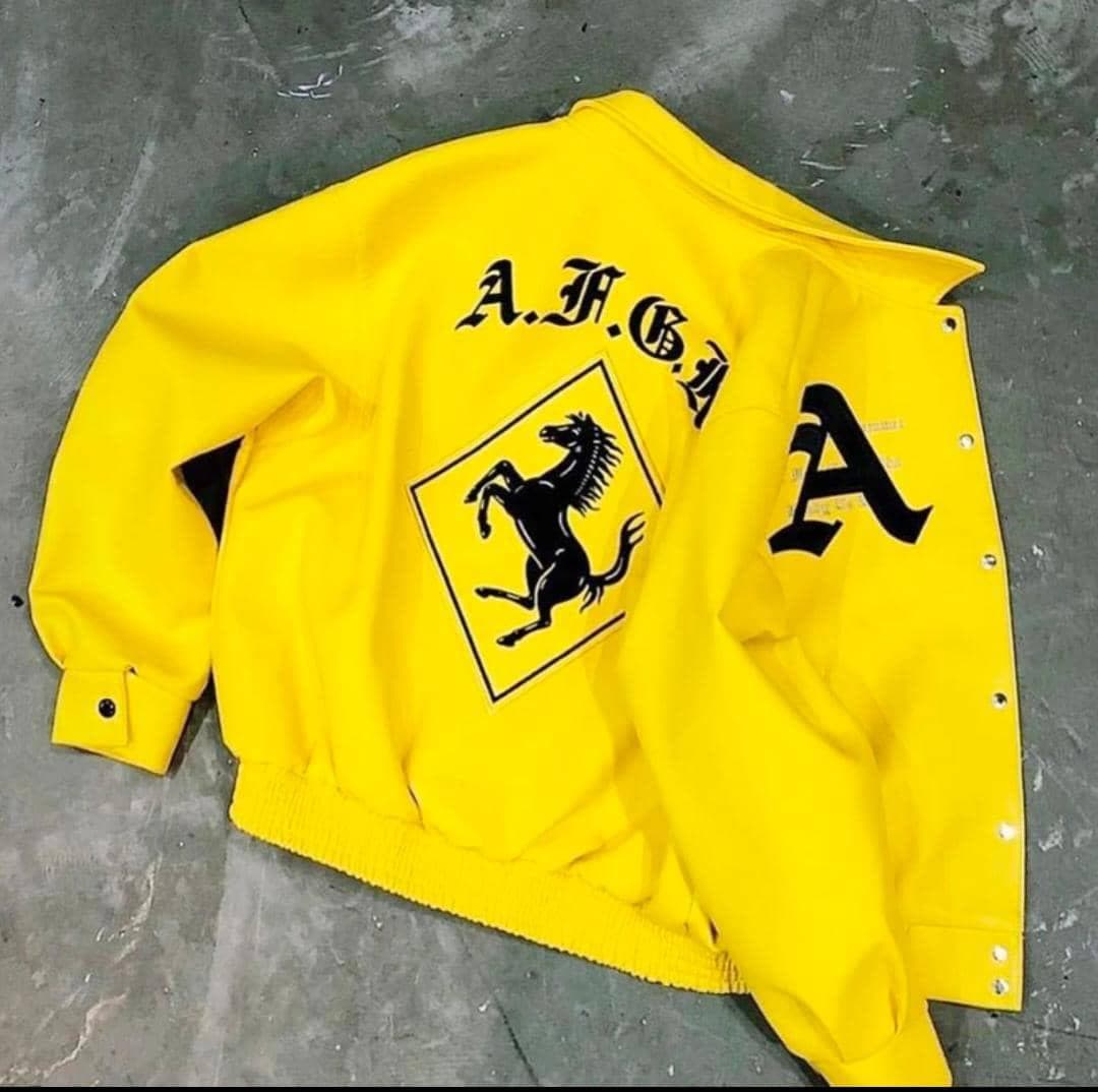 Yellow bomber jacket laid flat on concrete showing A.F.G.A text, prancing horse graphic and side details.