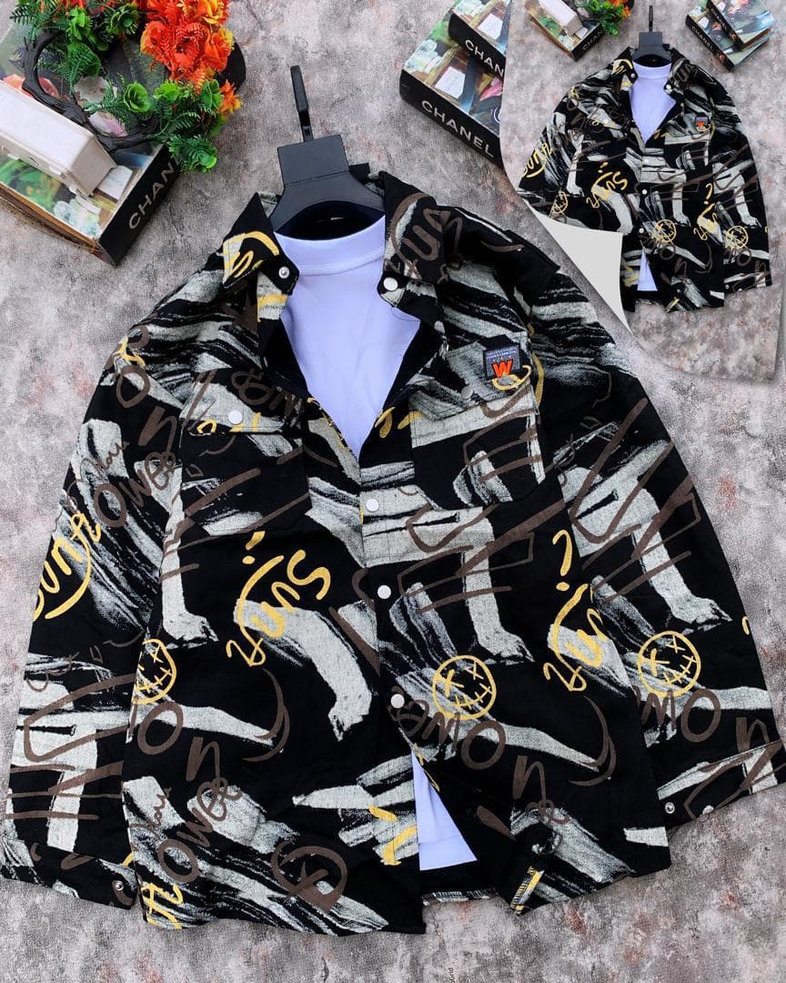 Black denim jacket with yellow and brown graffiti brushstroke print displayed on hanger over white t-shirt.