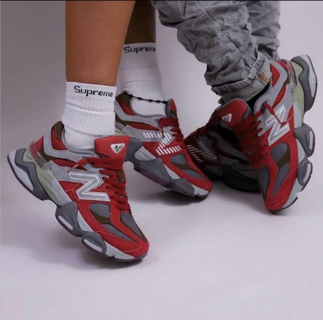 Person wearing red gray New Balance chunky sneakers paired with white Supreme socks.
