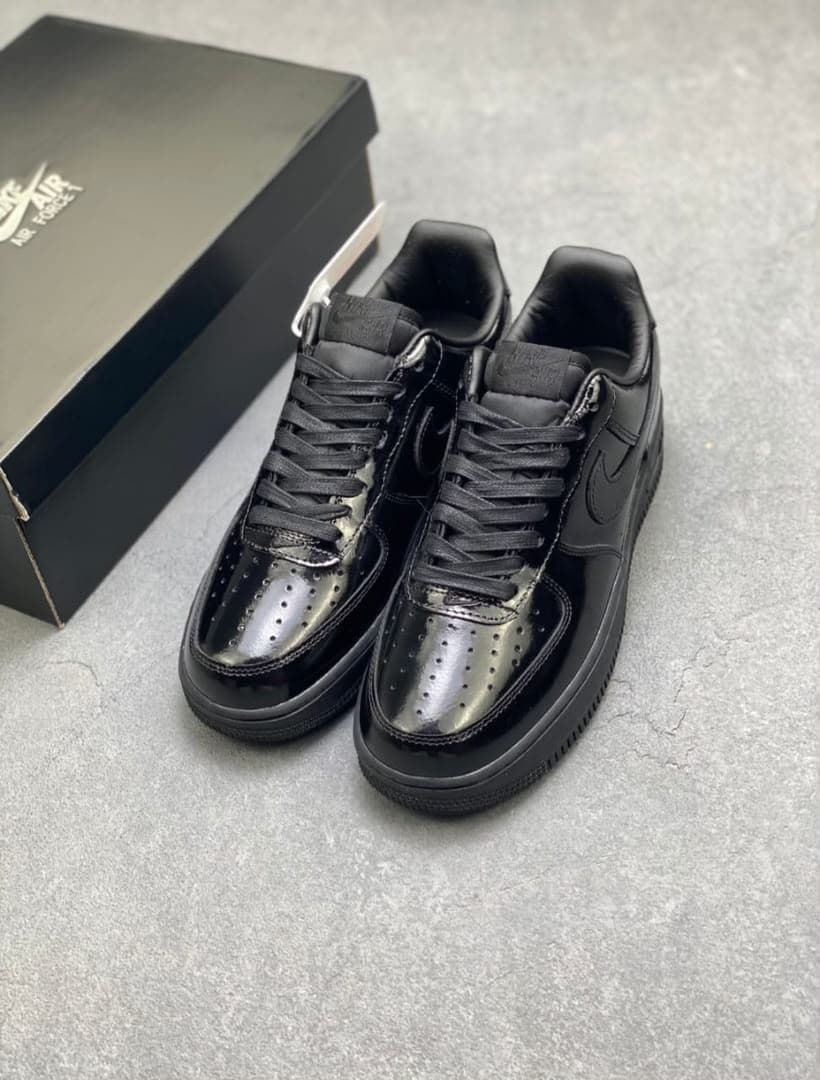 Pair of black patent leather Nike Air Force 1 sneakers beside black shoebox.