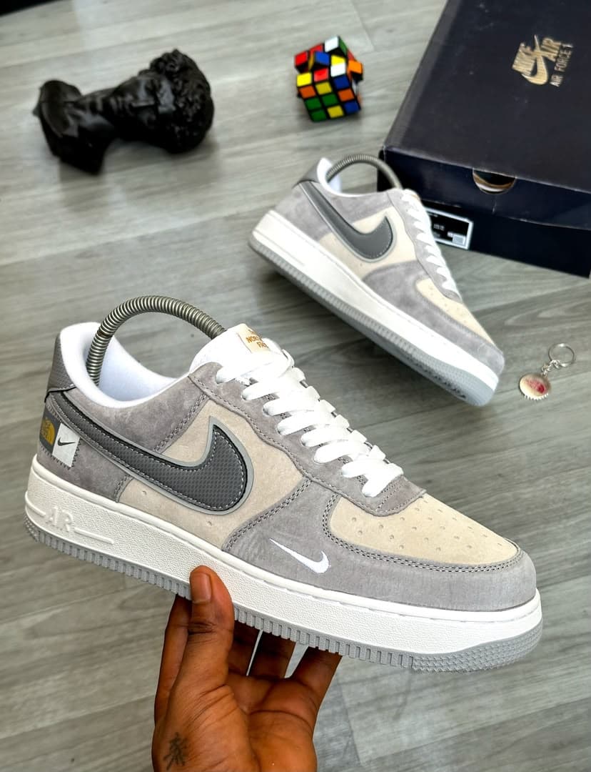 Grey and beige Nike Air Force 1 Low with The North Face patch held in hand.