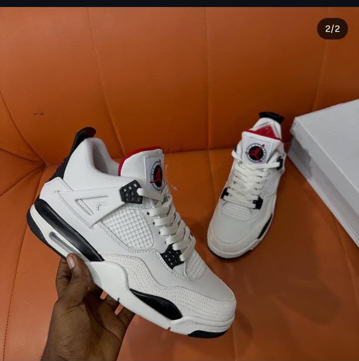 White, black and red Air Jordan 4 Retro sneaker held in hand on orange couch.