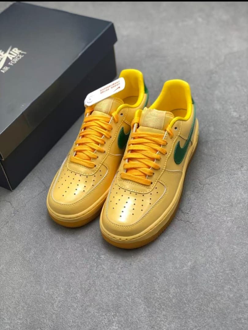 Pair of yellow Nike Air Force 1 sneakers with green swoosh and orange laces beside a shoebox.