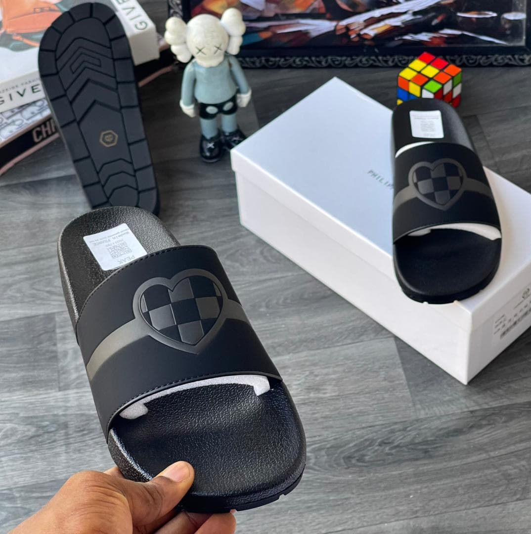 Black Philipp Plein slides with heart design held in foreground.