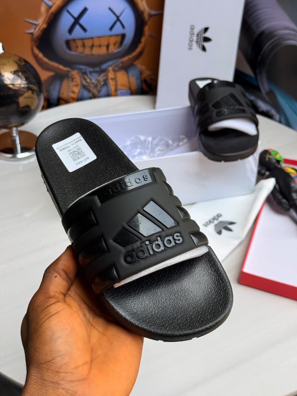 Black Adidas slides held close-up showing logo and details.