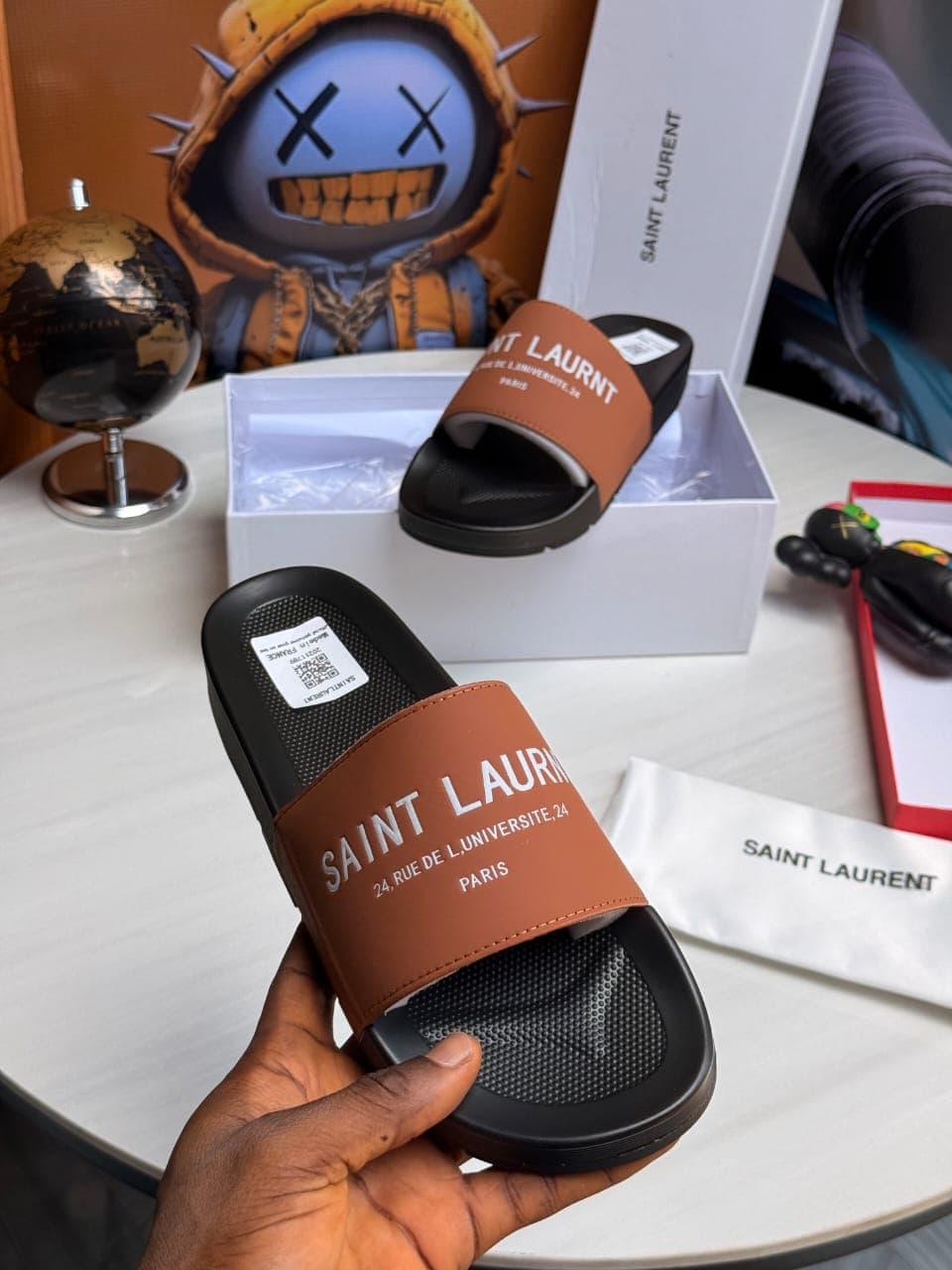 Brown Saint Laurent slides held displaying text and branding.