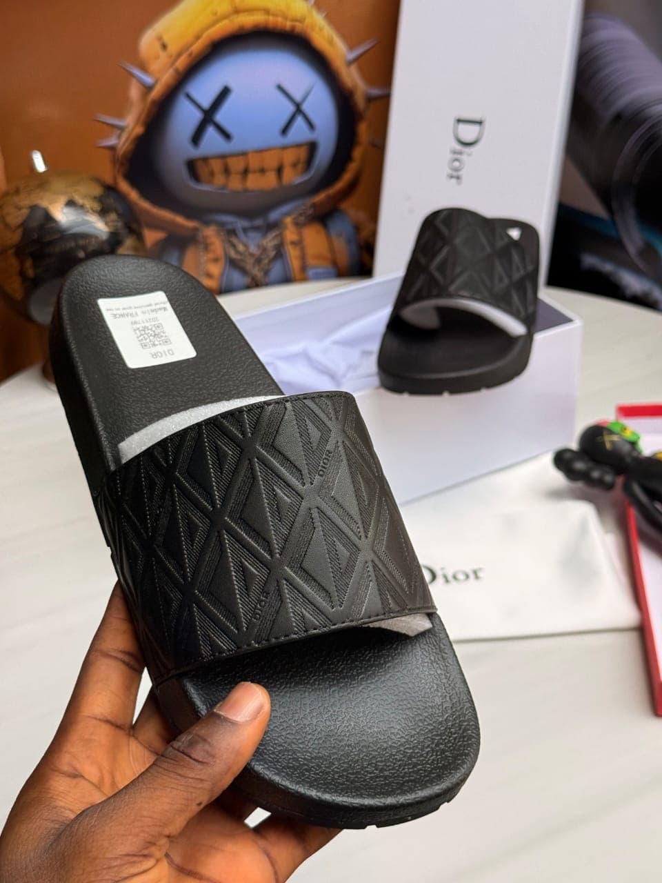 Black Dior slides held showing textured pattern and logo.