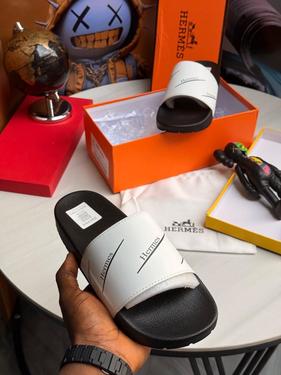 White Hermes slides held showing branding and orange box in background.