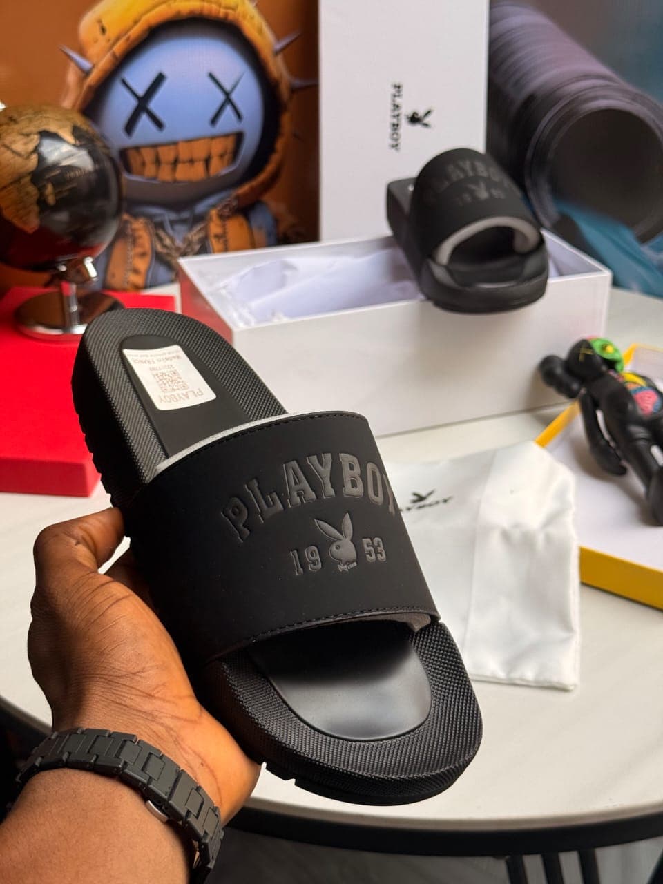Black Playboy slides held in hand displaying embossed logo and text.