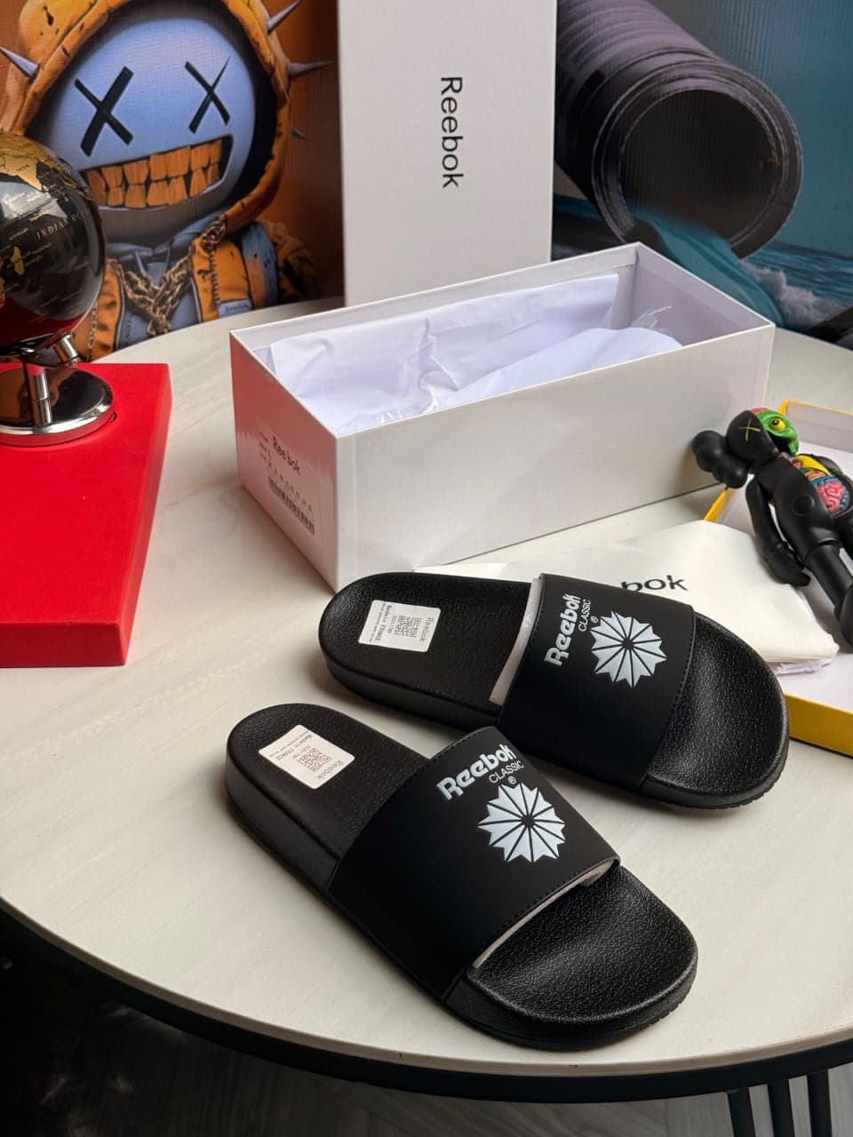 Pair of black Reebok Classic slides displayed on table with branding visible.