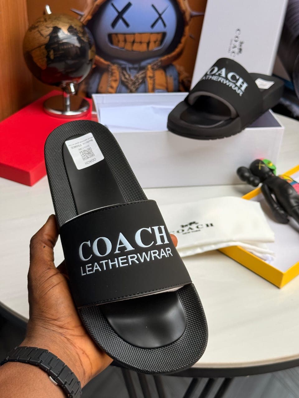 Black Coach slides with white branding held showing top view and logo.