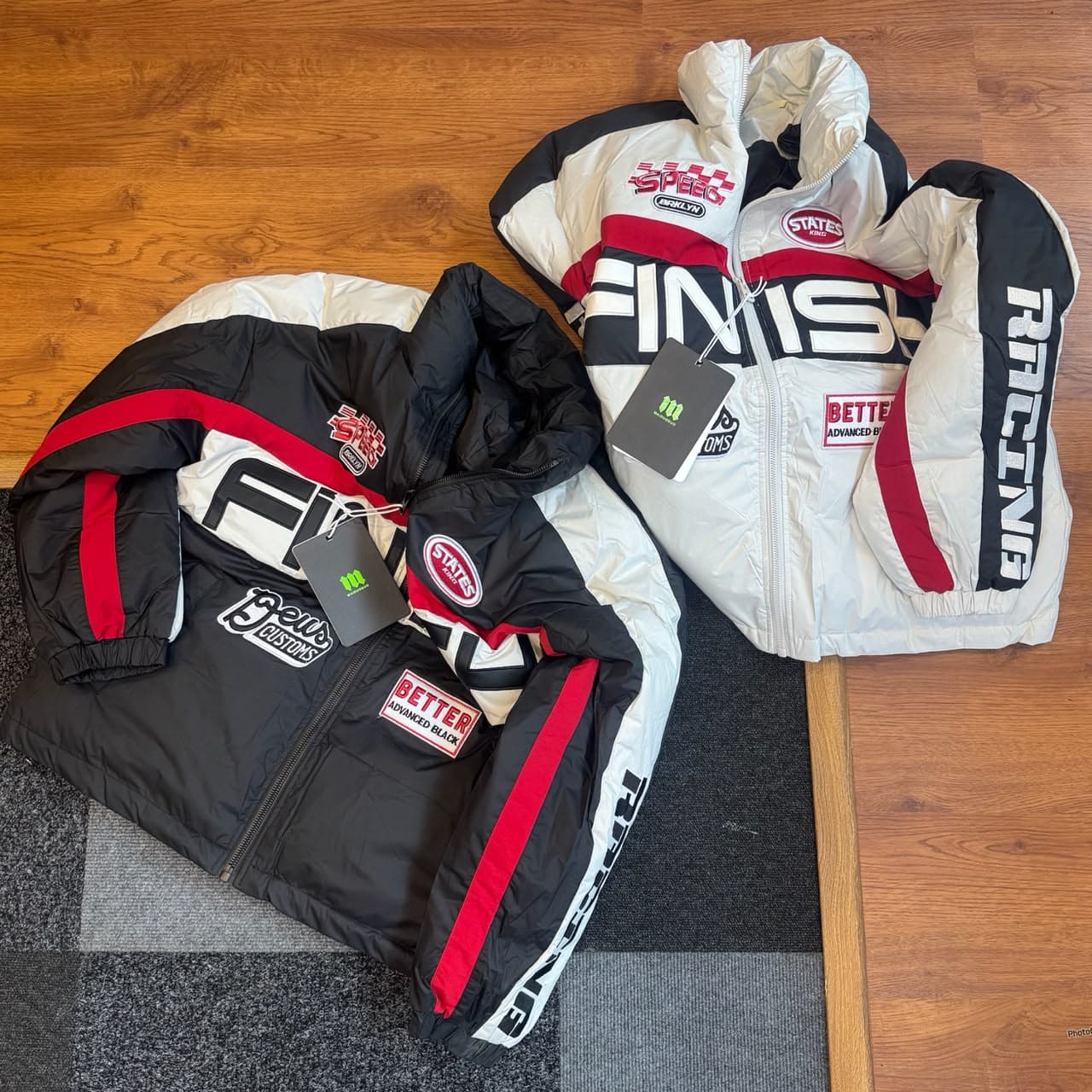Two racing puffer jackets in black and white colorways laid flat showing front graphics and details.