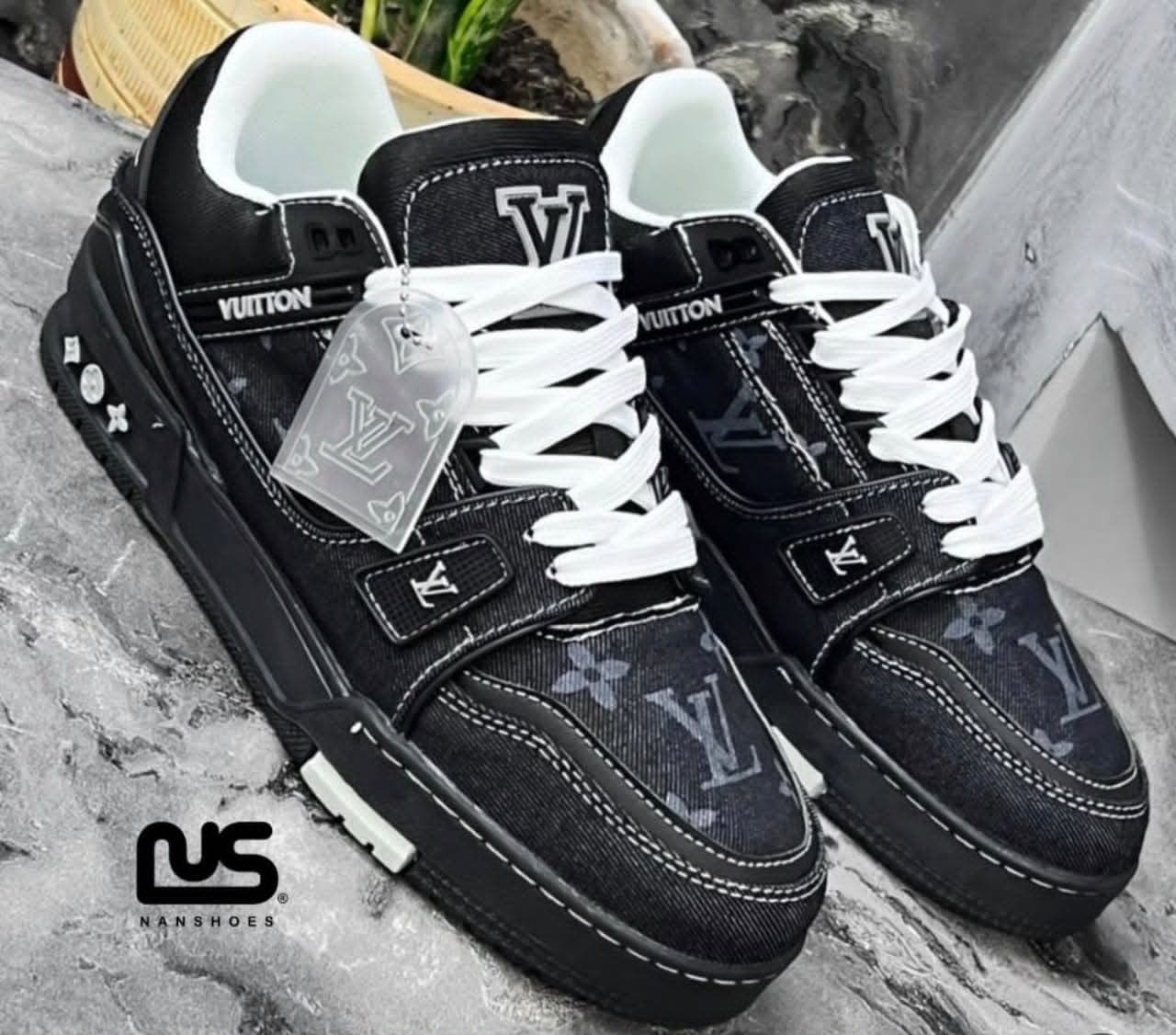 Black Louis Vuitton denim sneakers with monogram pattern and white accents displayed on textured surface.