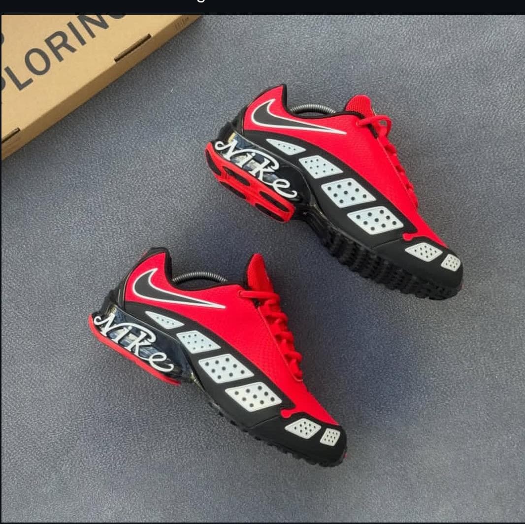 Red and black Nike Air Max Plus sneakers with dice pattern details on gray surface.