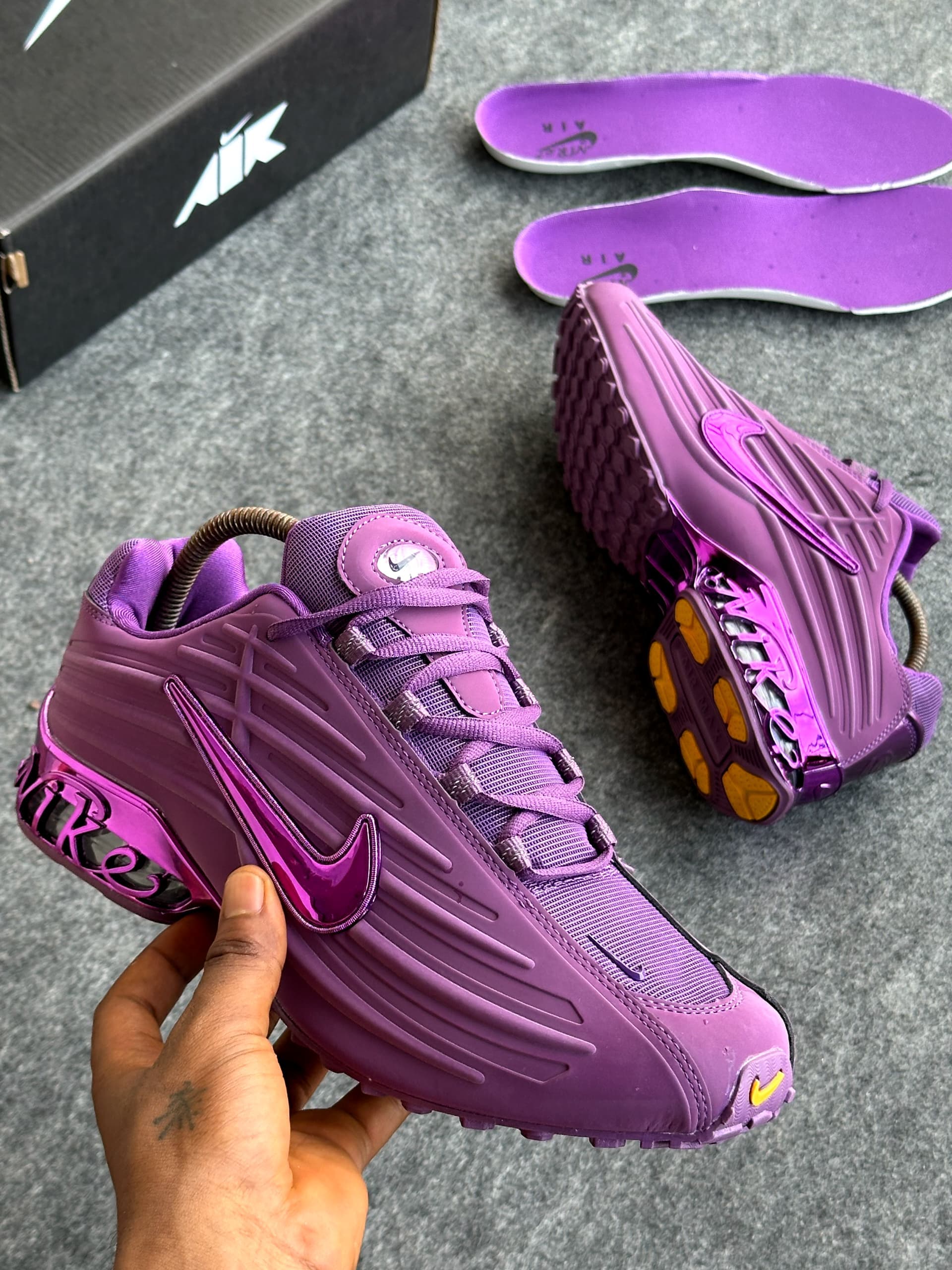 Purple Nike Air Max Plus sneakers held in hand with purple insoles and box.